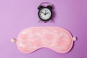 Sleeping eye mask, alarm clock isolated on purple violet pastel colourful trendy background. Do not disturb me, let me sleep. Rest, good night, siesta, insomnia, relaxation, tired, travel concept. photo