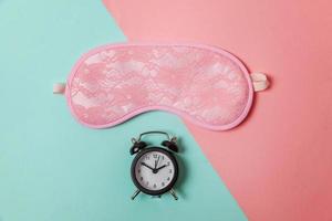 Sleeping eye mask, alarm clock isolated on blue pink pastel colorful trendy geometric background Do not disturb me, let me sleep. Rest, good night, siesta, insomnia, relaxation, tired, travel concept. photo