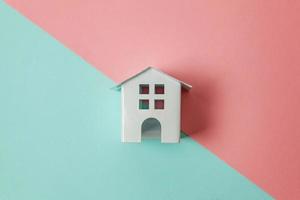 Simply design with miniature white toy house isolated on blue pink pastel colorful trendy geometric background. Mortgage property insurance dream home concept. Flat lay top view copy space. photo