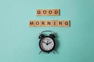 reloj de alarma de diseño simplemente plano e inscripción buenos días letras palabra sobre fondo azul pastel colorido de moda. hora del desayuno. buenos días despertar despierto concepto. espacio de copia de la vista superior. foto