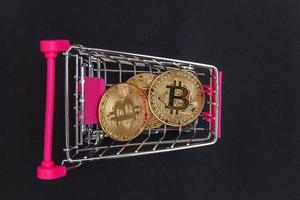 Cryptocurrency golden bitcoin coin in shopping cart on black background. Electronic virtual money for web banking and international network payment. Symbol of crypto virtual currency. Mining concept. photo