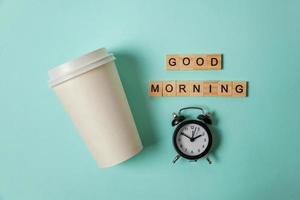 Simply flat lay design paper coffee cup and alarm clock on blue pastel colorful trendy background. Takeaway drink and breakfast beverage. Good morning wake up awake concept. Top view copy space. photo