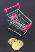 Cryptocurrency golden bitcoin coin and shopping cart on black background. Electronic virtual money for web banking and international network payment. Symbol of crypto virtual currency. Mining concept. photo