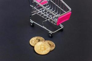 Cryptocurrency golden bitcoin coin and shopping cart on black background. Electronic virtual money for web banking and international network payment. Symbol of crypto virtual currency. Mining concept. photo