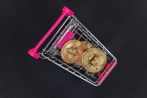 Cryptocurrency golden bitcoin coin in shopping cart on black background. Electronic virtual money for web banking and international network payment. Symbol of crypto virtual currency. Mining concept. photo