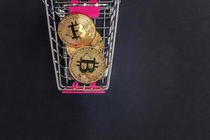 Cryptocurrency golden bitcoin coin in shopping cart on black background. Electronic virtual money for web banking and international network payment. Symbol of crypto virtual currency. Mining concept. photo