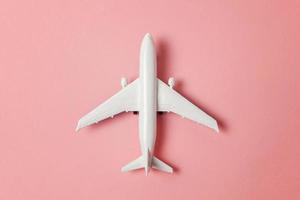 Simply flat lay design miniature toy model plane on pink pastel colorful paper trendy background. Travel by plane vacation summer weekend sea adventure trip journey ticket tour concept. photo