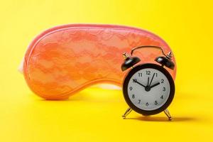 Sleeping eye mask, alarm clock isolated on yellow colourful trendy modern fashion background. Do not disturb me, let me sleep. Rest, good night, siesta, insomnia, relaxation, tired, travel concept. photo