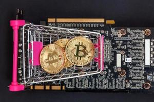 Cryptocurrency golden bitcoin coin lying in shopping cart and video card. Electronic virtual money for web banking and international network payment. Symbol of crypto virtual currency. Mining concept. photo