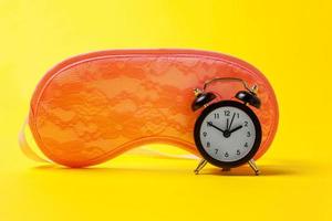 Sleeping eye mask, alarm clock isolated on yellow colourful trendy modern fashion background. Do not disturb me, let me sleep. Rest, good night, siesta, insomnia, relaxation, tired, travel concept. photo