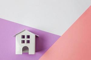 Simply design with miniature white toy house isolated on white violet pink pastel colorful trendy geometric background. Mortgage property insurance dream home concept. Flat lay top view copy space. photo