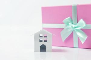 casa de juguete blanca en miniatura y caja de regalo envuelta en papel rosa aislado sobre fondo blanco. concepto de casa de ensueño de seguro de propiedad hipotecaria. comprar casa nueva para la familia. foto
