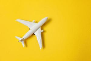 Simply flat lay design miniature toy model plane on yellow colorful paper trendy background. Travel by plane vacation summer weekend sea adventure trip journey ticket tour concept. photo