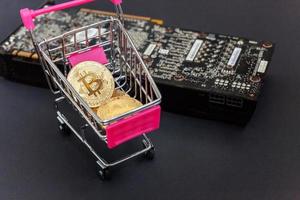 Cryptocurrency golden bitcoin coin lying in shopping cart and video card. Electronic virtual money for web banking and international network payment. Symbol of crypto virtual currency. Mining concept. photo