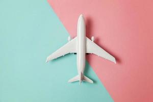 Simply flat lay design miniature toy model plane on blue and pink pastel colorful paper trendy geometric background. Travel by plane vacation summer weekend sea adventure trip concept. photo