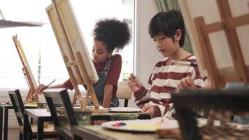 Eine Gruppe gemischtrassiger kleiner Kinder konzentriert sich in einem Kunstklassenzimmer auf das Malen von Acrylbildern auf Leinwand und lernt kreativ mit Talenten und Fähigkeiten in der Studioausbildung der Grundschule. video