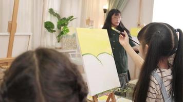 A group of multiracial kids learning with a female Asian teaches acrylic color picture painting on canvas in art classroom, creatively learning with skill at the elementary school studio education. video