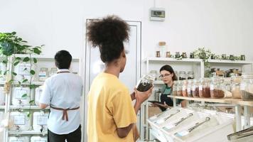 A female shopkeeper describes natural organic products to Black woman customer in refill store, zero-waste and plastic-free grocery, environment-friendly, sustainable lifestyles with a reusable shop. video