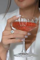 A vertical shot of a Caucasian female holding a cocktail glass with a ring on the finger photo