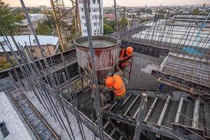 The workers on a building infrastructure roof with machinery and tools. Pouring concrete into a mold photo