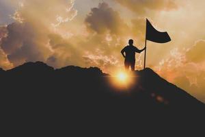 silueta de una mujer de negocios con banderas en la cima de una montaña sobre el cielo y la luz del sol foto