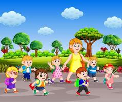 the children going to school with their teacher walking on the street in the sunny day vector