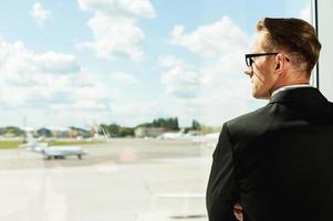 Waiting for his flight. Rear view of thoughtful businessman in formalwear looking through a window in airport photo