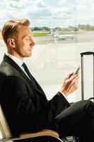 Waiting for his flight. Side view of confident businessman in formalwear holding mobile phone while waiting for a flight in airport photo