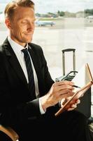 Businessman making notes. Side view of confident businessman in formalwear writing something in note pad while waiting for a flight in airport photo