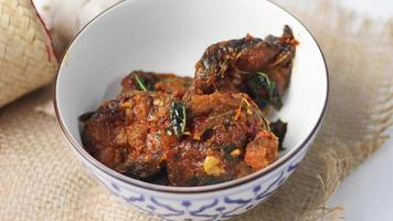 Spicy Stir Fried Catfish served in a Thai style patterned bowl on a white table. photo