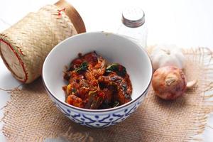 Spicy Stir Fried Catfish served in a Thai style patterned bowl on a white table. photo