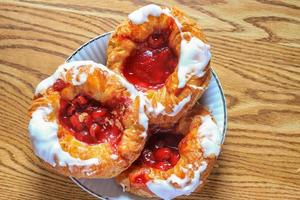 Cherry filled Danish or Danish bread served in a white plate on a brown wooden table. photo