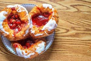 pan danés o danés relleno de cereza servido en un plato blanco sobre una mesa de madera marrón. foto