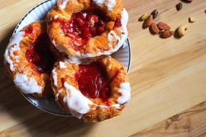 Cherry filled Danish or Danish bread served in a white plate on a brown wooden table. photo