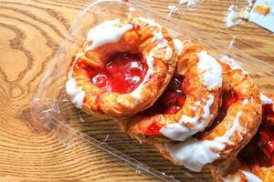 Cherry filled Danish or Danish bread in a plastic box placed on a brown wooden table. photo