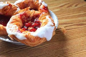 Cherry filled Danish or Danish bread served in a white plate on a brown wooden table. photo