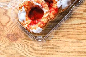 Cherry filled Danish or Danish bread in a plastic box placed on a brown wooden table. photo