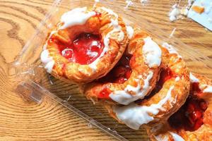 Cherry filled Danish or Danish bread in a plastic box placed on a brown wooden table. photo