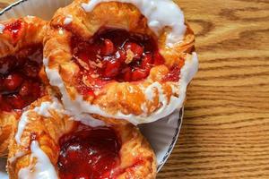 Cherry filled Danish or Danish bread served in a white plate on a brown wooden table. photo