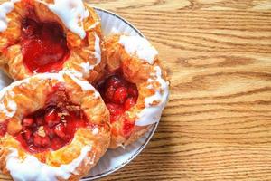 Cherry filled Danish or Danish bread served in a white plate on a brown wooden table. photo