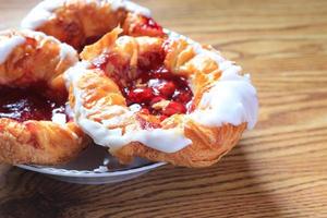 Cherry filled Danish or Danish bread served in a white plate on a brown wooden table. photo