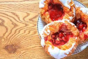 Cherry filled Danish or Danish bread served in a white plate on a brown wooden table. photo