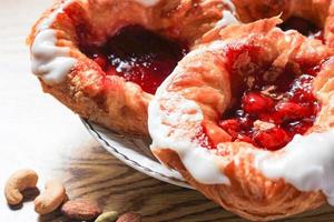 pan danés o danés relleno de cereza servido en un plato blanco sobre una mesa de madera marrón. foto