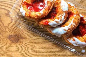 Cherry filled Danish or Danish bread in a plastic box placed on a brown wooden table. photo