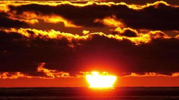 puesta de sol rojo carmesí en la costa del mar. pintoresca puesta de sol brillante a través de nubes oscuras video
