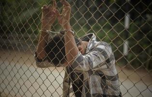 close-up photo of hands in prison steel mesh handle Handles the steel mesh cage, lacks independence.