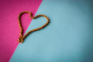Texture of a beautiful golden festive chain unique weaving in the shape of a heart on a pink purple blue background and copy space. Concept love, marriage proposal, marriage, St. Valentine's Day photo