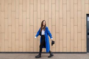 stylish woman in a blue autumn coat walks around the city against the background of a beige wall photo