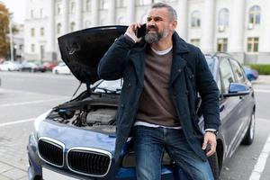 a man next to a broken car calls the rescue service photo