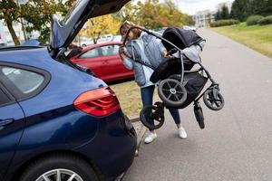 a young woman loads a stroller into the trunk of a car photo